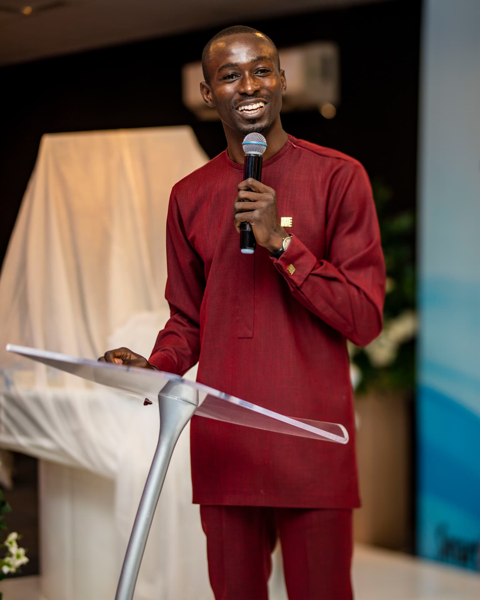 King David Amo speaking with a handheld microphone at a clear acrylic lectern