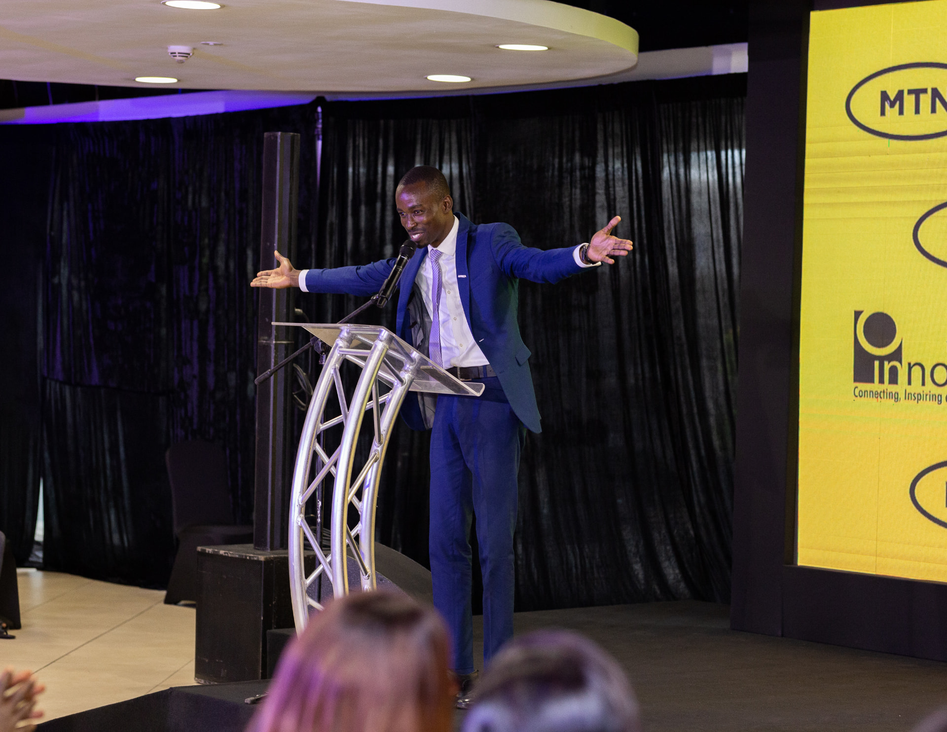 King David Amo hosting on stage with arms open, addressing the audience at a corporate innovation event